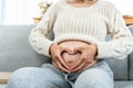 Close-up of Asian pregnant woman's hand posing in heart shape on big belly Sitting on sofa in the living room of house