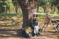 Close up Asian woman in casual wear sitting and working with a laptop under the tree next to a white bicycle in a public park Royalty Free Stock Photo