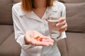 Close up Asian woman holding pill and a glass of water sitting on sofa