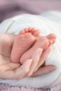 Close up asian woman mother hand holding small baby infant feet while sleeping on soft bed covered with white cloth. Royalty Free Stock Photo