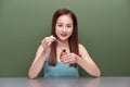 Close up asian woman 20s with perfect skin, nude make up apply oil from bottle on face isolated on green wall background