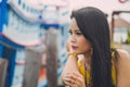 Close Up Asian Woman In A Yellow Dress Put Her Chin On Her Hand Looking Away At A Bay With Sea Boat Blurred Background