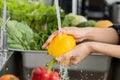 Close up asian young housekeeper woman, washing sweet pepper, yellow paprika, vegetables with splash water in basin on sink in Royalty Free Stock Photo