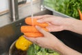 Close up asian young woman washing carrot, tomato, broccoli fresh vegetables, paprika with splash water in basin of water on sink