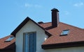 A close-up of an asphalt shingled roofing construction with attic skylights, a chimney, soffit, fascia board and roof gutters