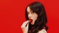 Close up of attractive brunette sexy woman enjoying a taste of fresh strawberry on a colorful red background