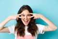 Close up of attractive excited woman showing v-signs, disco gesture near eyes, smiling pleased, standing upbeat against