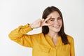 Close-up of attractive and healthy young woman smiling, showing peace kawaii sign on eye, standing over white background Royalty Free Stock Photo