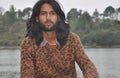 Close-up of a attractive Indian young guy with long hair and beard looking at camera while sitting by the lake Royalty Free Stock Photo