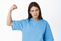 Close up of attractive young girl acting tough, flexing biceps, showing muscles on raised arm and looking serious