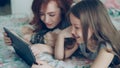 Close-up of attractive young mother and her cute daughter in pajamas laughing and looking in digital tablet while lying Royalty Free Stock Photo