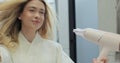 Close up of attractive young woman looking at her reflection in the mirror and drying hair with blow dryer in bathroom Royalty Free Stock Photo