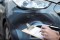 Close Up Of Auto Workshop Mechanic Inspecting Damage To Car And Filling In Repair Estimate