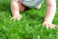 Close-up baby crowling through green grass lawn. Details infant hand walking in park . Child discovering and exploring Royalty Free Stock Photo