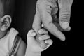 CLOSE-UP BABY`S OR CHILD HAND HOLDING ELDERLY FINGER OF GRANDFATHER. BLACK AND WHITE SHOT