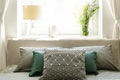 Close-up of the back of the bed with gray and green pillows against a sunny window with a lamp and a bunch of wild flowers on the Royalty Free Stock Photo