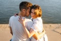 Close-up back view of beautiful young happy couple in love hugging, sitting on bench on city waterfront near river in Royalty Free Stock Photo