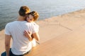 Close-up back view of happy young couple hugging each other sitting on bench on city waterfront near river in sunny Royalty Free Stock Photo