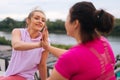 Close-up back view of positive fitness female trainer and motivated fat young woman greeting each other with high-five