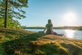 Close up back view of woman relaxing and enjoys warm evening Sunset on flat stone slope close to river. Scandinavian nature