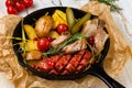 Close-up baked potatoes, krakow sausage, tender breast, pork knuckle, pickled cucumber, cherry tomatoes on black frying pan, lunch