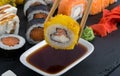 Close-up, baked roll in tempura, wooden sticks are lowered into a container with soy sauce, against a background of assorted Royalty Free Stock Photo