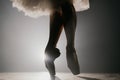 Close up of ballet dancer as she practices exercises on dark stage or studio. Woman`s feet in pointe shoes. Ballerina