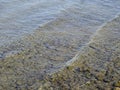 Close up of Baltic sea ripple on water surface with sunlight reflecting on a sunny day. Small smooth brown stones Royalty Free Stock Photo