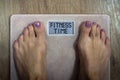 Close up of bare female feet standing on bathroom scale with written words Fitness time on display. Concept of shaping and