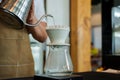 Close-up barista hand holding kettle raised pour coffee powder, address in device for drip coffee drink brewed coffee while done,