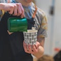 Close-up of barista hands, preparing a hot milk foam, pourin milk in paper cup with coffee cappuccino. Professional