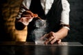 Close-up. Bartender holds in hand tweezers with ice over steaming glass