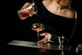 Close-up bartender girl pours finished cold cocktail from mixing cup into glass Royalty Free Stock Photo