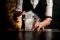 Close-up. Bartender holds in hand tweezers with ice and puts it in steaming glass