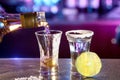 Close-up of a bartender pouring golden tequila into a glass with salt and lime