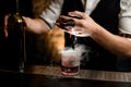 Close-up. Bartender`s hand gently pours smoky drink from jigger into glass with ice Royalty Free Stock Photo