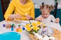 Close up of basket with Easter eggs and toy-rabbit. Defocused teacher and toddler girl are painting egg at th background Royalty Free Stock Photo