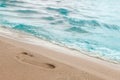 Close-up of the beach shore with a man`s footprint on the yellow sand along the line of the blue sea wave on a summer sunny day. Royalty Free Stock Photo