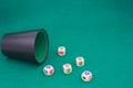 A beaker with poker dice on a green table