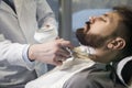 Close up of a bearded brown haired businessman sitting at a barber shop in a chair.