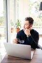 Close up of a bearded businessman glasses in hand and sitting at his laptop and look in the window.