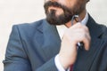 Close up of bearded chin hand holds glasses of businessman in suit and red tie. Businessman think over with hand near of his chin.