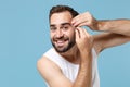 Close up bearded young man 20s years old in white shirt hold in hand tweezers isolated on blue pastel background, studio