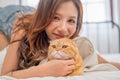Close up beautiful Asian woman lie near her orange cat also scratch the chin of cat to make it relax and she also look at camera Royalty Free Stock Photo