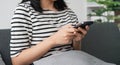 Close up of beautiful Asian woman sit on sofa hand holding mobile phone chatting with friends and playing social media Royalty Free Stock Photo