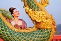 Close up beautiful Asian woman with Thai traditional dress stand behide the naga sculpture in temple area with morning light