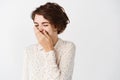 Close up of beautiful brunette female in blouse laughing, cover mouth while chuckle from joke, standing against white