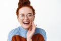 Close up of beautiful candid woman with ginger hair combed in bun, wearing glasses, laughing and smiling sincere