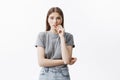 Close up of beautiful caucasian student girl with dark hair in trendy grey clothes holding hand near mouth, looking in Royalty Free Stock Photo