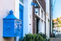 A close-up of a beautiful deep blue dutch mailbox decorated with a bas-relief with a street view at the background.